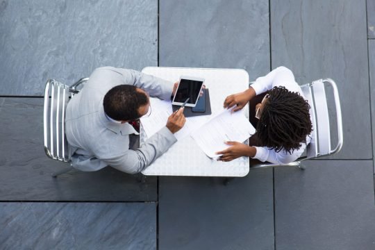 African American man pointing on tablet. Top view of two business people looking at tablet. Business meeting concept